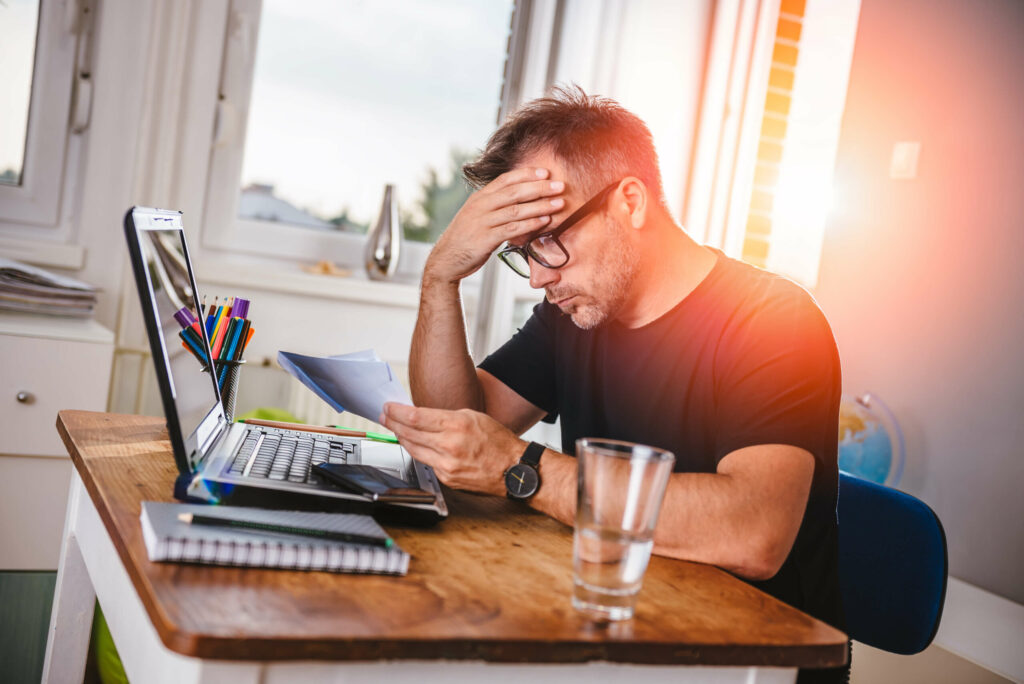 Man sitting in home office, reading letter and felling worried. With one hand holding letter and with other his forehead
