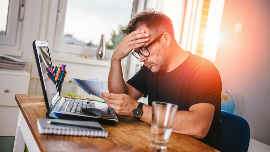 Man sitting in home office, reading letter and felling worried. With one hand holding letter and with other his forehead