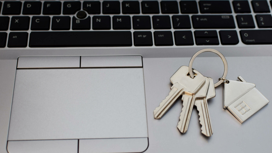 Three metal keys with keychain and house shape pendant on grey laptop with black keyboard.  Online house rental or purchasing concept.